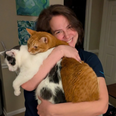 Katrina smiling while holding two cats