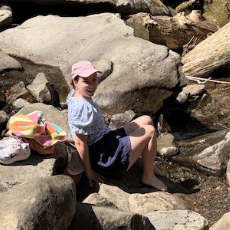 Lydia sitting on rocks by a stream
