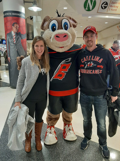 Team member and husband standing with Stormy, the Carolina Hurricanes mascot.