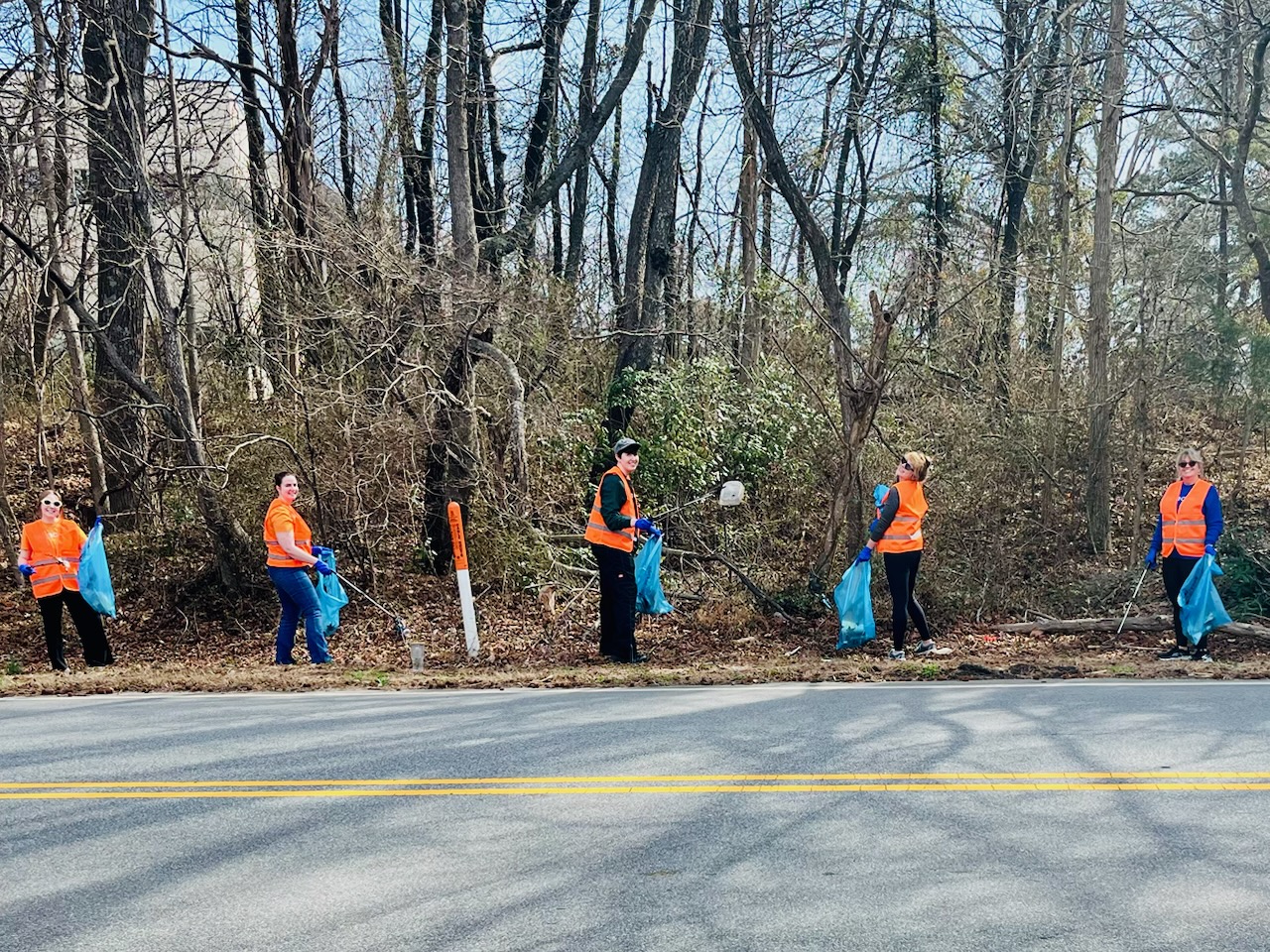 Beacon team members in orange vests clean up trash along the side of the road.