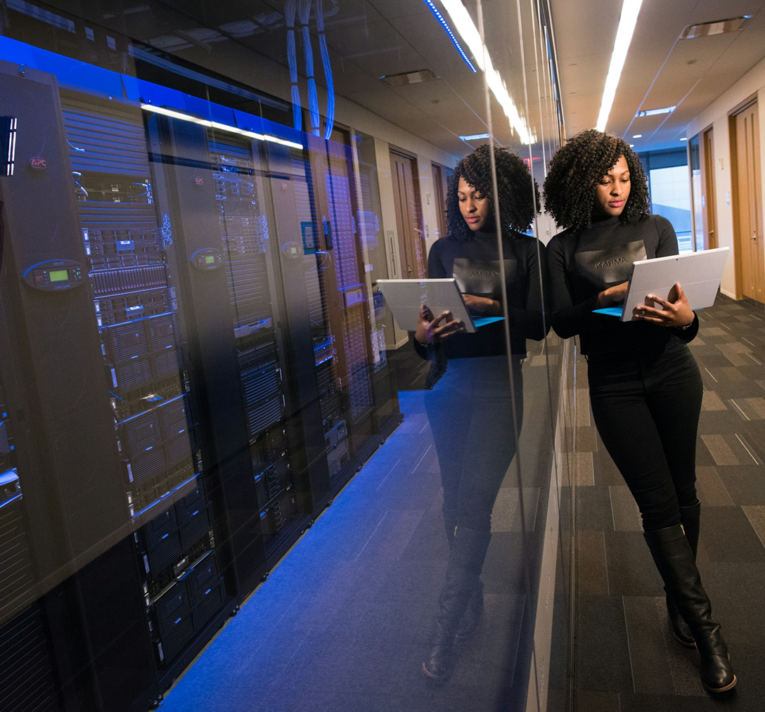 woman working on a laptop leaning against a server wall 