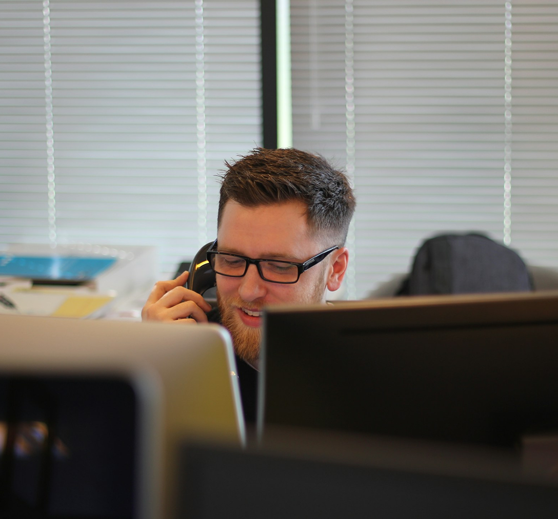 smiling man on the phone with a customer sitting behind a row of computers