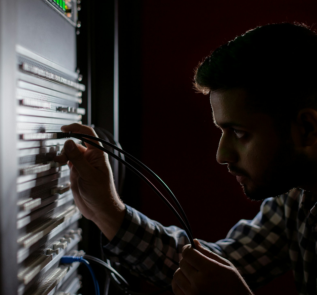 man examining a server wall where things are plugged in