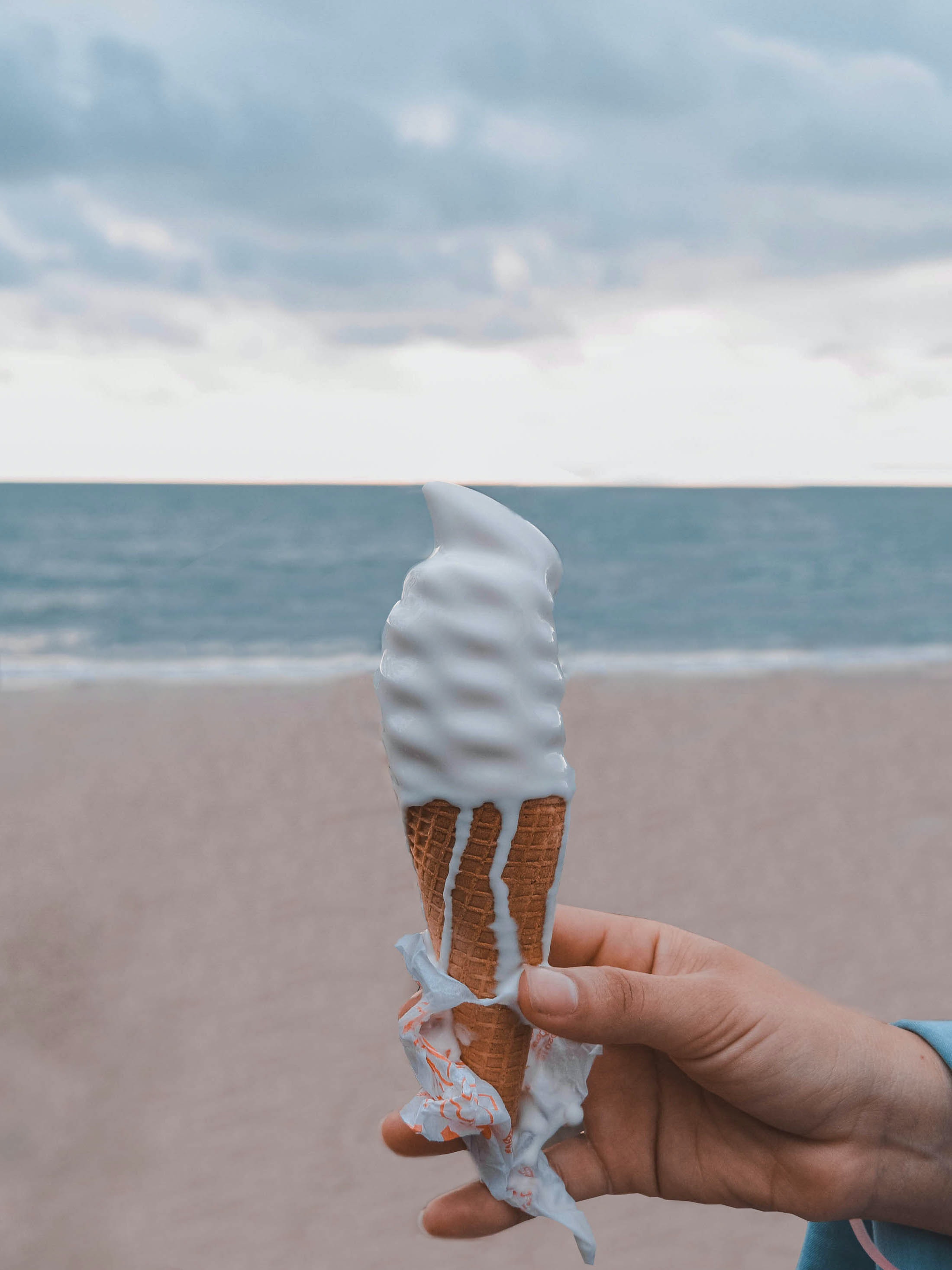 person holding vanilla ice cream cone on the beach