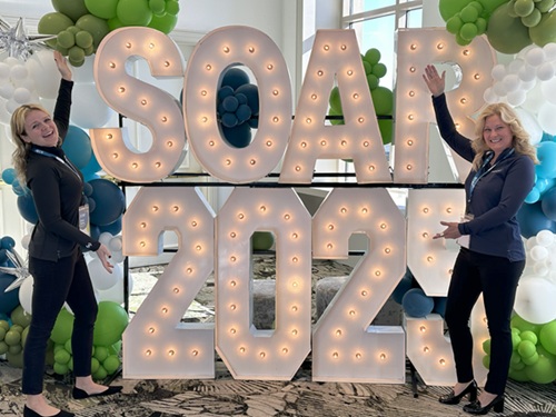 Beacon team posing in front of a large SOAR 2025 tradeshow display